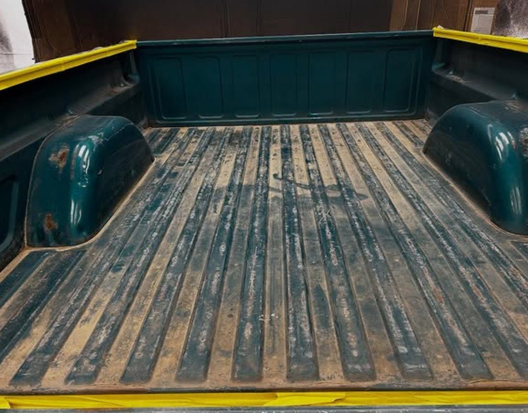 A worn truck bed with bare, scraped metal before coating